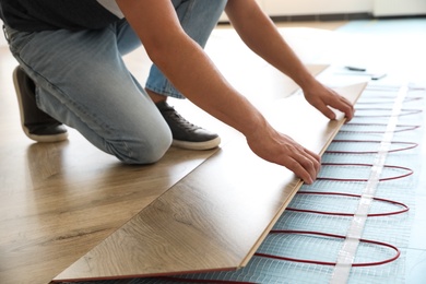 Photo of Professional contractor installing underfloor trace heating system indoors, closeup