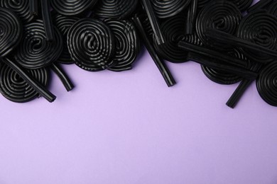 Tasty black liquorice candies on violet background, flat lay. Space for text