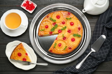 Delicious cut pineapple pie with cherry and tea served on black wooden table, flat lay