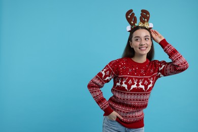 Photo of Young woman in Christmas sweater and reindeer headband on light blue background. Space for text