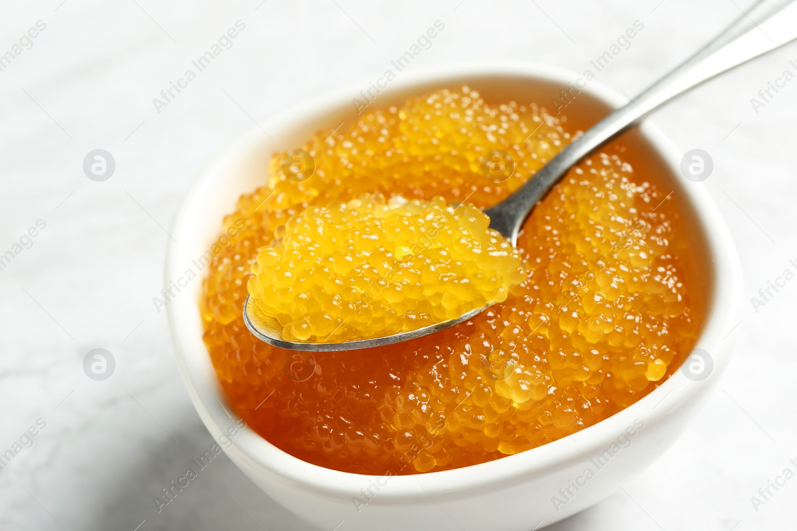 Photo of Fresh pike caviar in bowl and spoon on white table, closeup