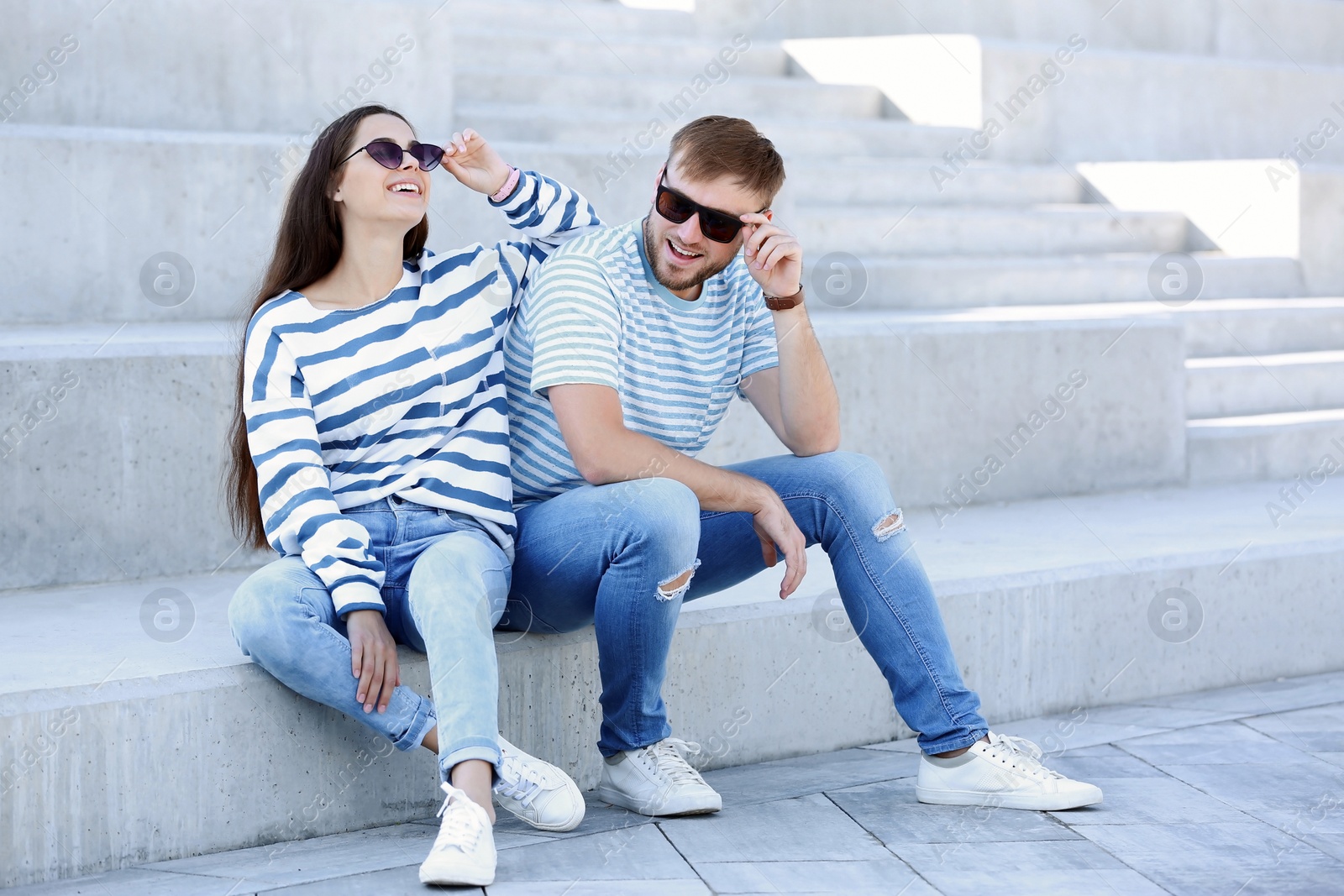 Photo of Young hipster couple in stylish jeans sitting on stairs outdoors