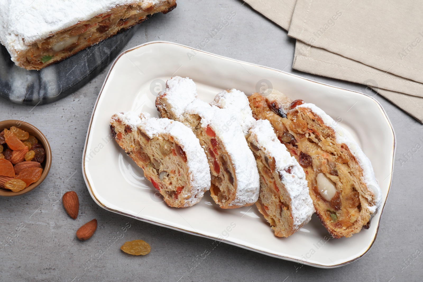 Photo of Traditional Christmas Stollen with icing sugar on grey table, flat lay