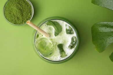 Photo of Glass of tasty iced matcha latte and powder on light green background, flat lay