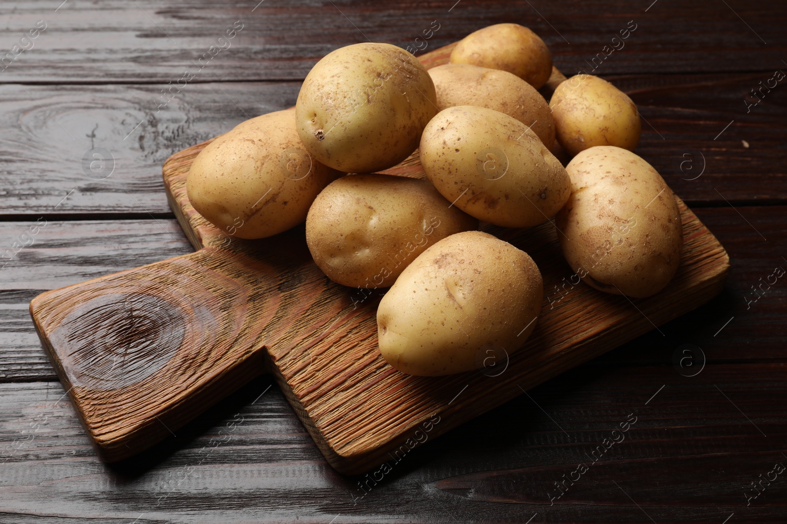 Photo of Raw fresh potatoes and cutting board on wooden table