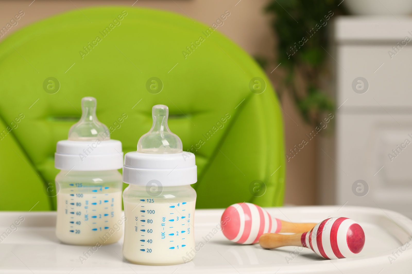 Photo of High chair with feeding bottles of infant formula and toy maracas on white tray indoors