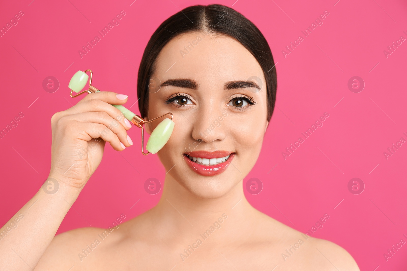 Photo of Woman using natural jade face roller on pink background