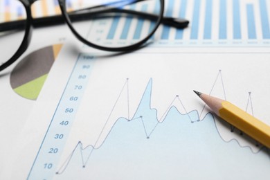 Glasses and pencil on accounting documents with graphs, closeup