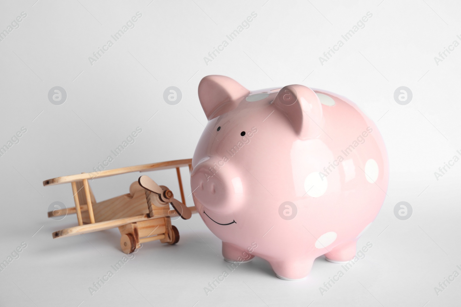 Photo of Piggy bank with toy airplane on light background. Travel agency