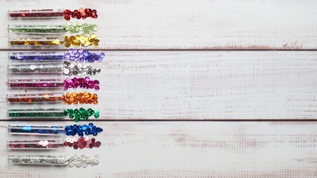 Tubes with many colorful sequins on white wooden table, flat lay. Space for text