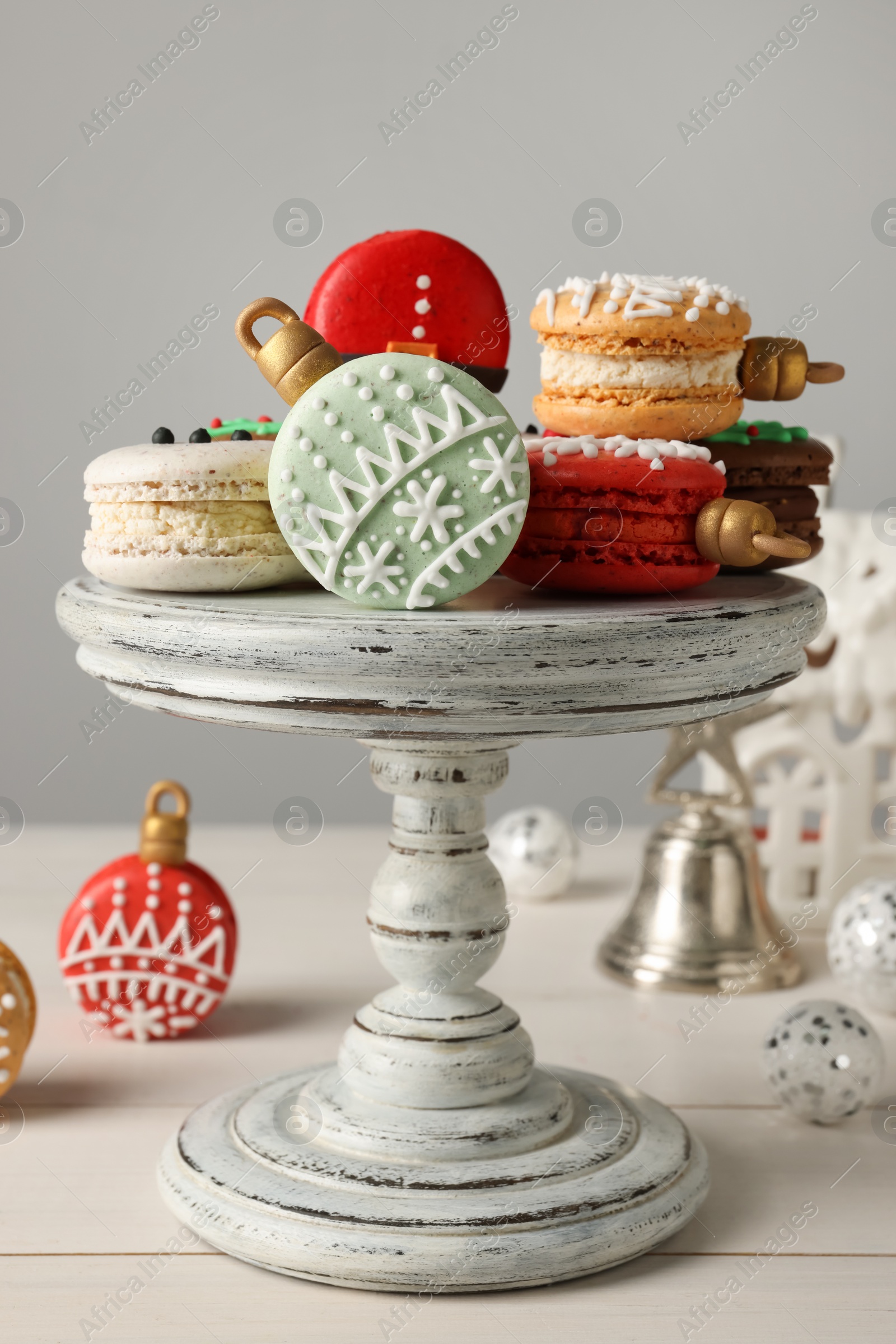 Photo of Stand with beautifully decorated Christmas macarons on white wooden table