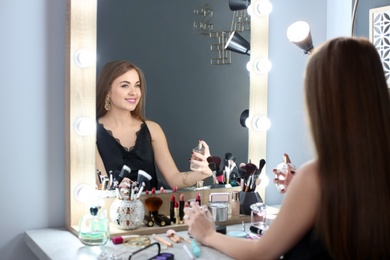 Photo of Young woman with makeup made by professional artist applying perfume in dressing room
