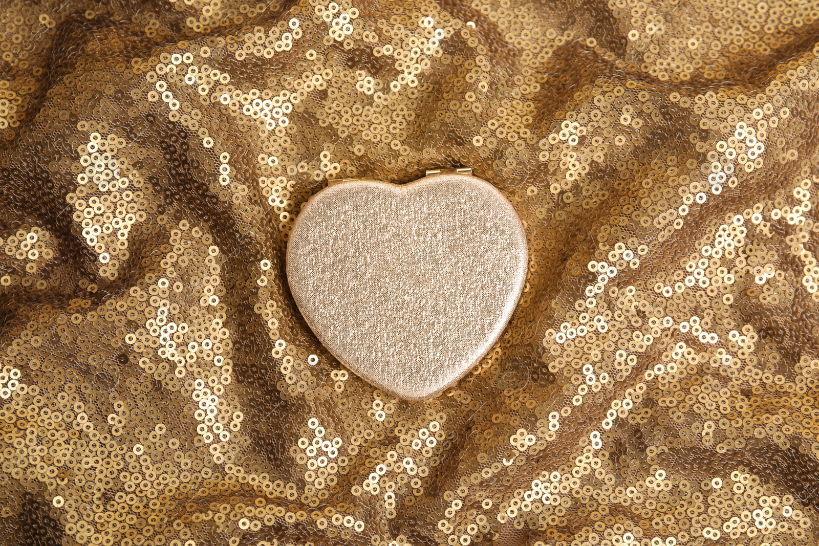 Photo of Stylish heart shaped cosmetic pocket mirror on gold fabric, top view