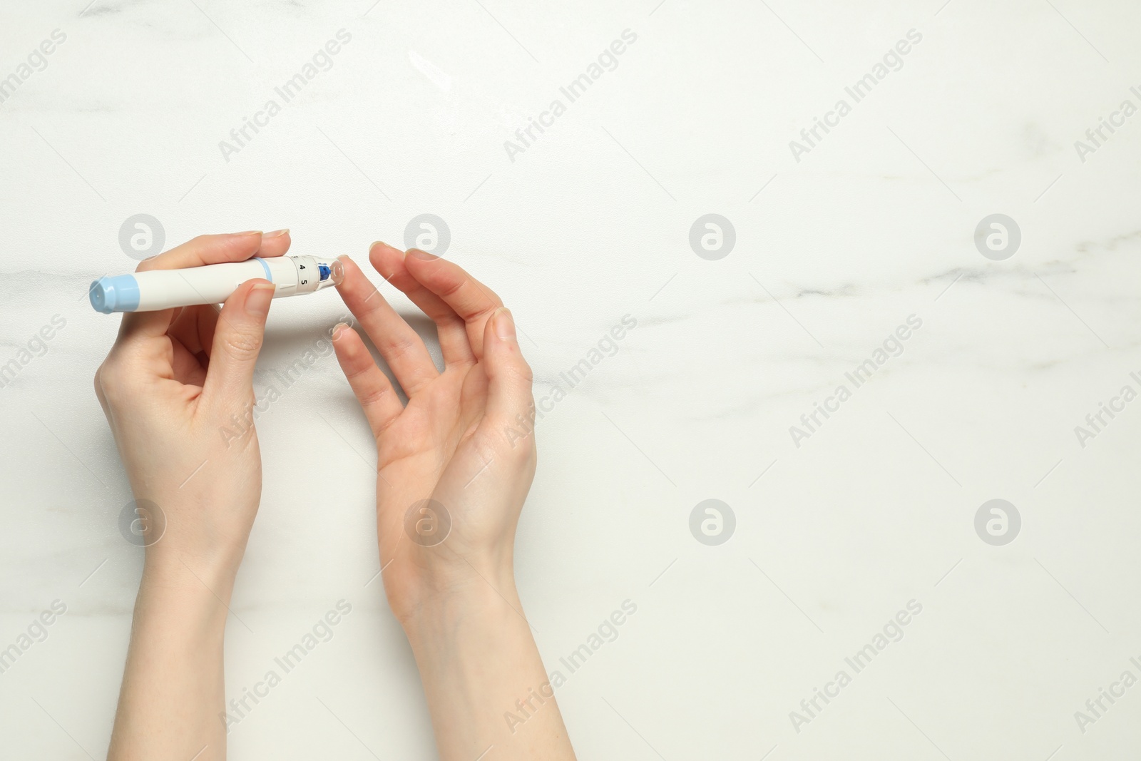 Photo of Diabetes. glucose testing. Woman using lancet pen at white marble table, top view. Space for text
