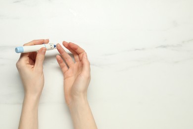 Diabetes. glucose testing. Woman using lancet pen at white marble table, top view. Space for text