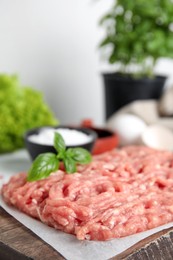 Photo of Raw chicken minced meat with basil on wooden board, closeup