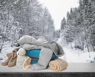 Image of Suitcase with warm clothes on stone surface against beautiful winter landscape