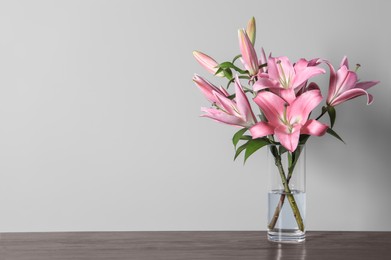 Photo of Beautiful pink lily flowers in vase on wooden table against light background, space for text