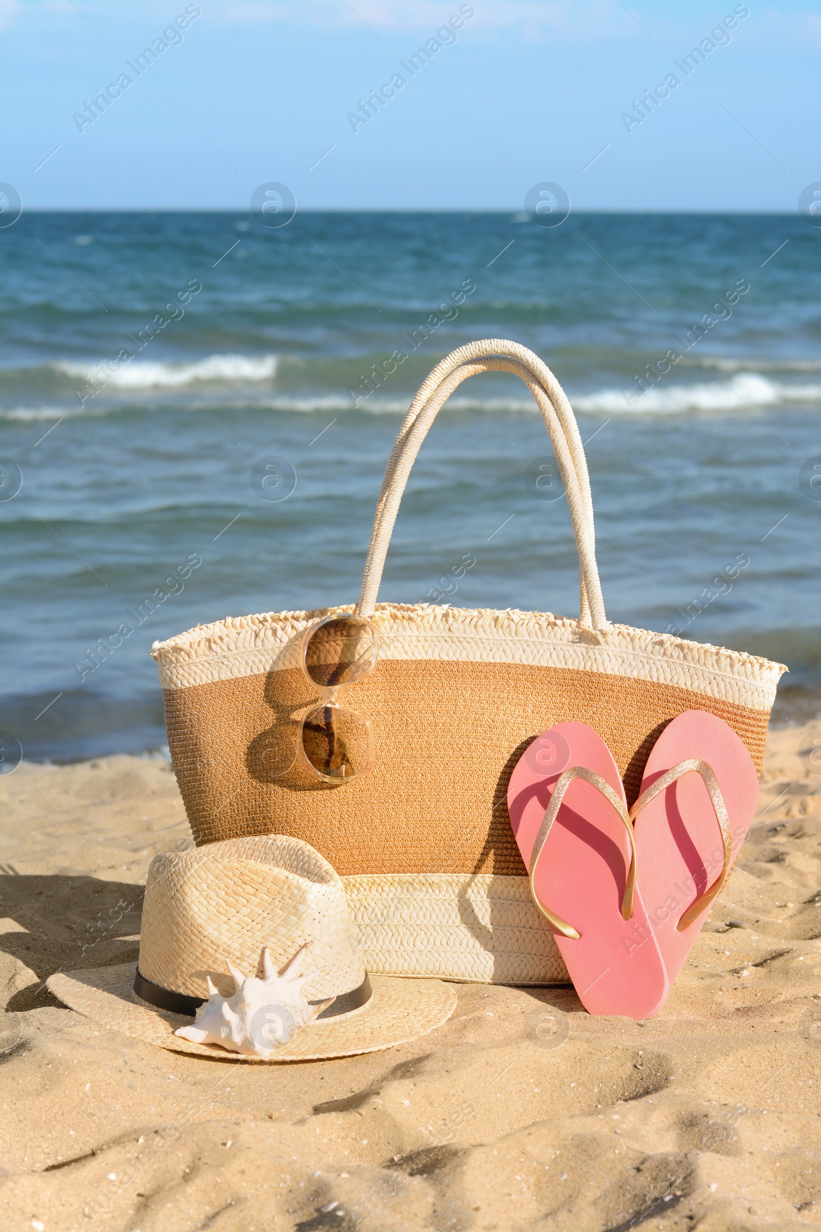 Photo of Stylish bag and other beach accessories near sea on sunny day