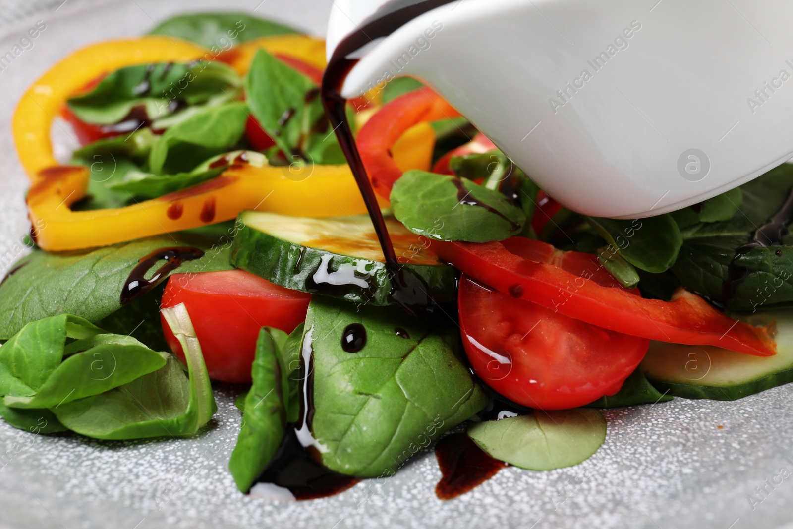 Photo of Pouring balsamic vinegar onto fresh vegetable salad on plate, closeup