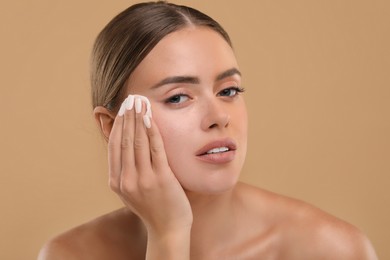 Photo of Beautiful woman removing makeup with cotton pad on beige background