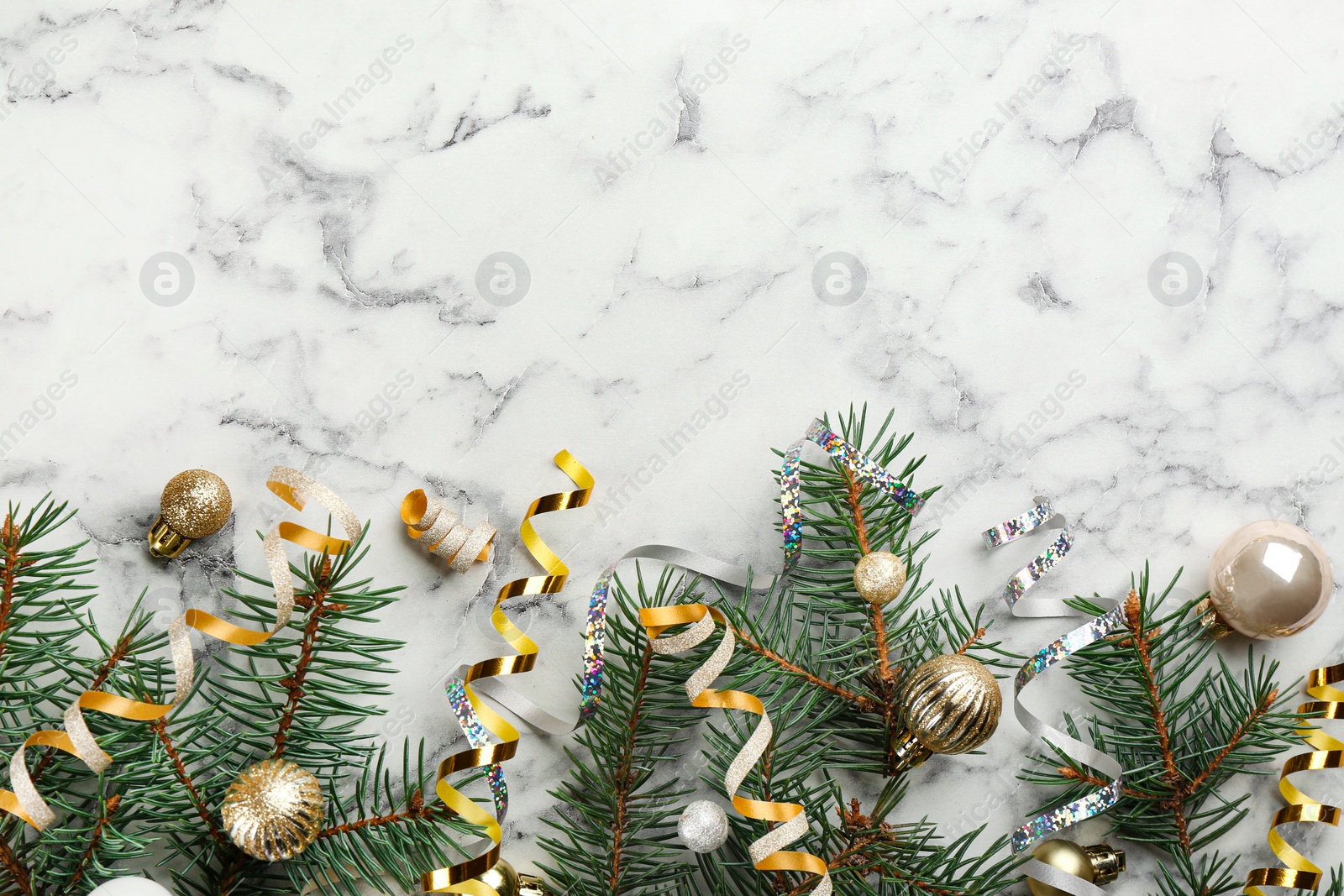 Photo of Shiny serpentine streamers, Christmas balls and fir branches on white marble background, flat lay. Space for text