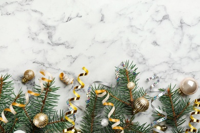 Photo of Shiny serpentine streamers, Christmas balls and fir branches on white marble background, flat lay. Space for text