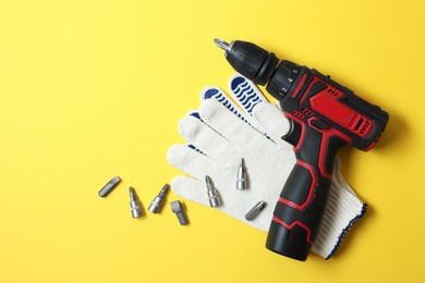 Photo of Electric screwdriver, bit set and gloves on yellow background, flat lay