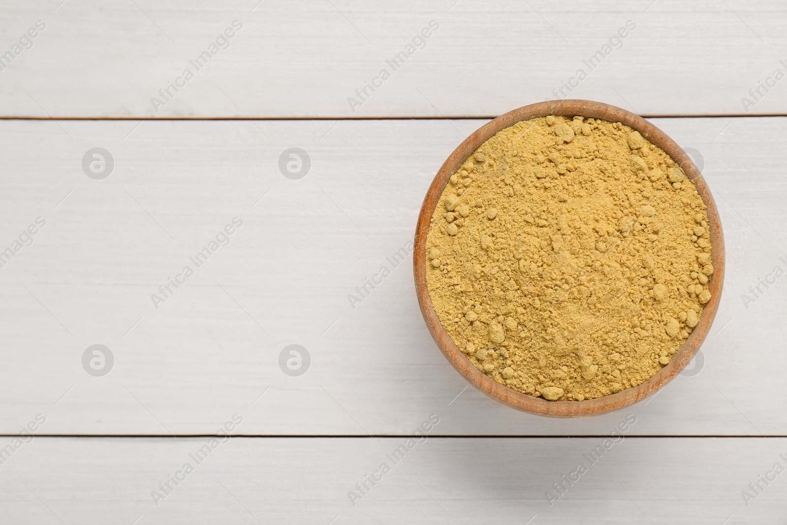 Photo of Bowl of aromatic mustard powder on white wooden table, top view. Space for text