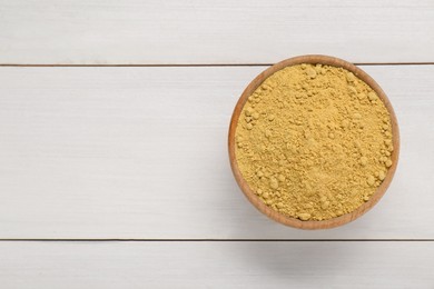 Photo of Bowl of aromatic mustard powder on white wooden table, top view. Space for text