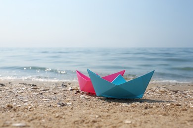 Bright paper boats on sandy beach near sea, space for text