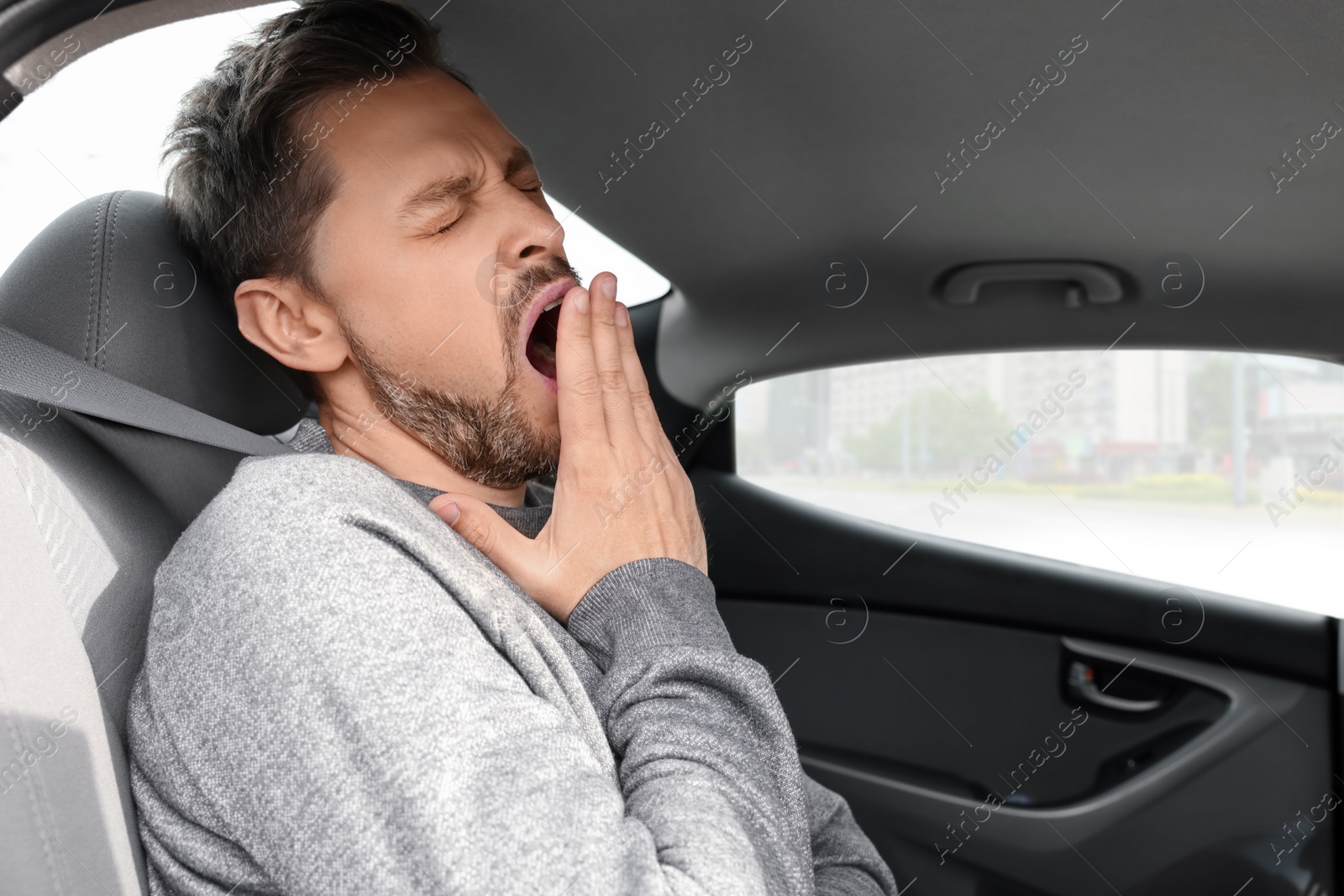Photo of Sleepy handsome man yawning while sitting in modern car