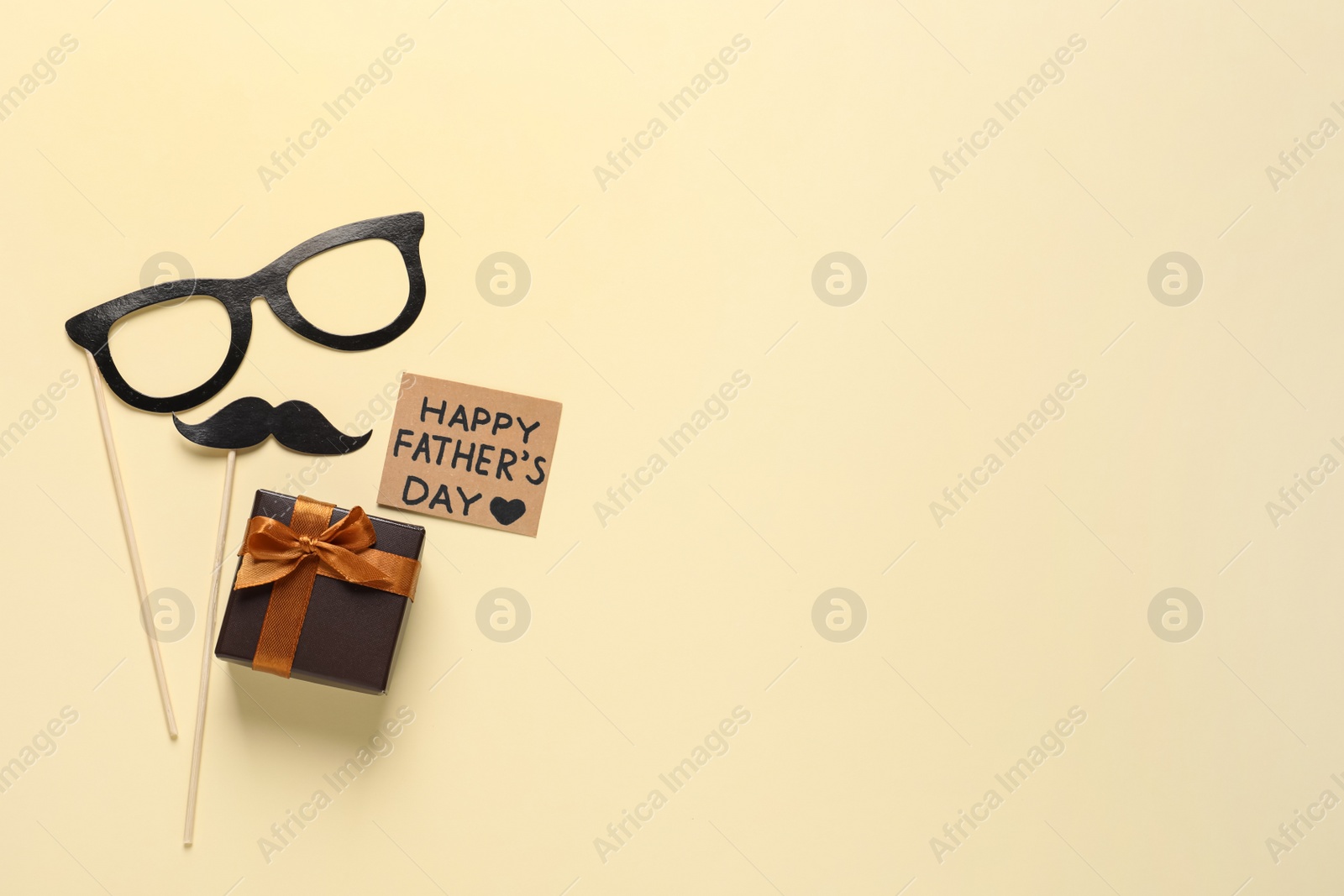 Photo of Card with phrase Happy Father's Day, paper glasses, mustache and gift box on pale yellow background, flat lay. Space for text