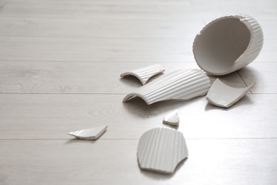 Photo of Broken white ceramic vase on wooden floor