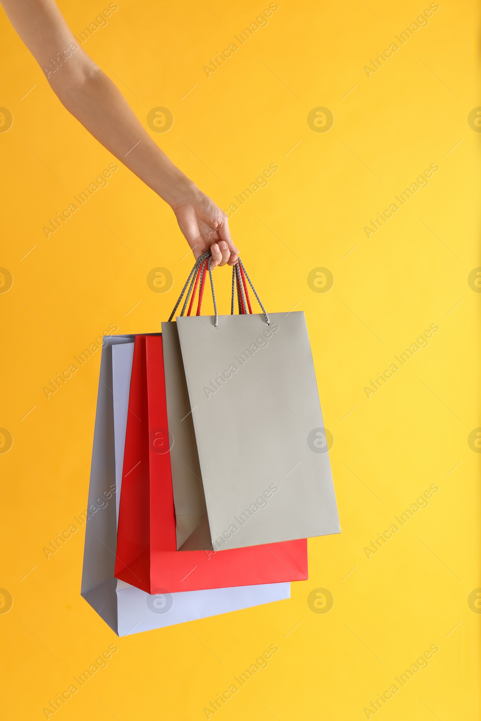 Photo of Woman with paper shopping bags on yellow background, closeup