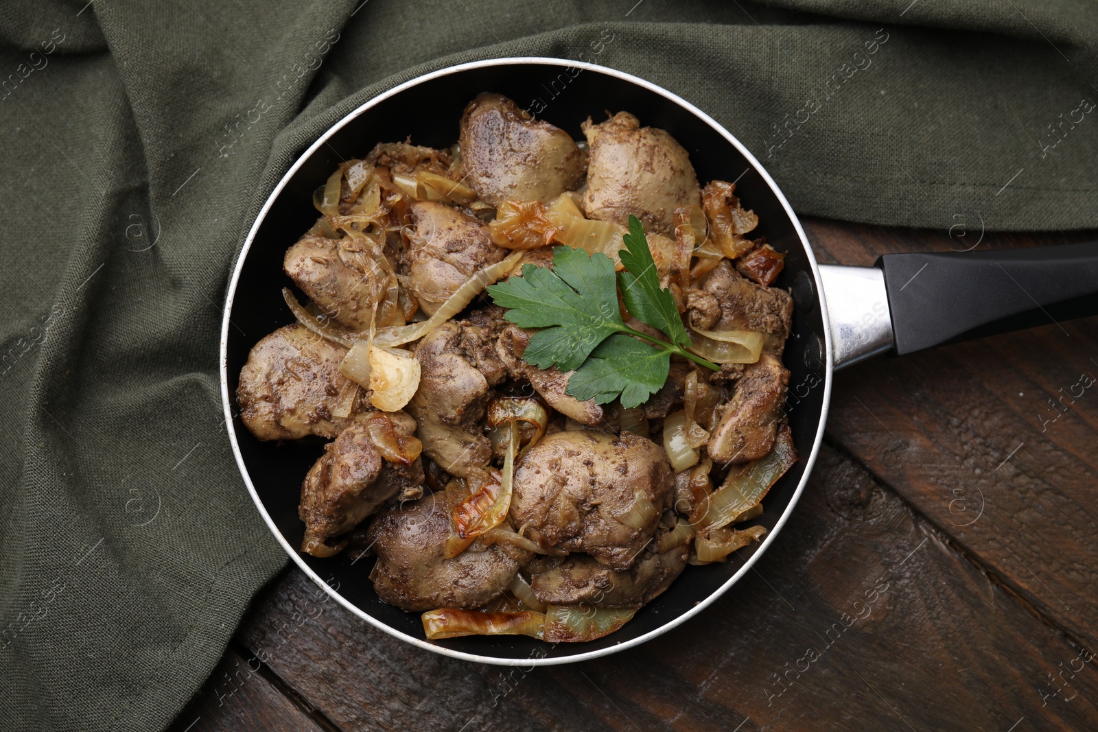 Photo of Pan with tasty fried chicken liver, onion and parsley on wooden table, top view