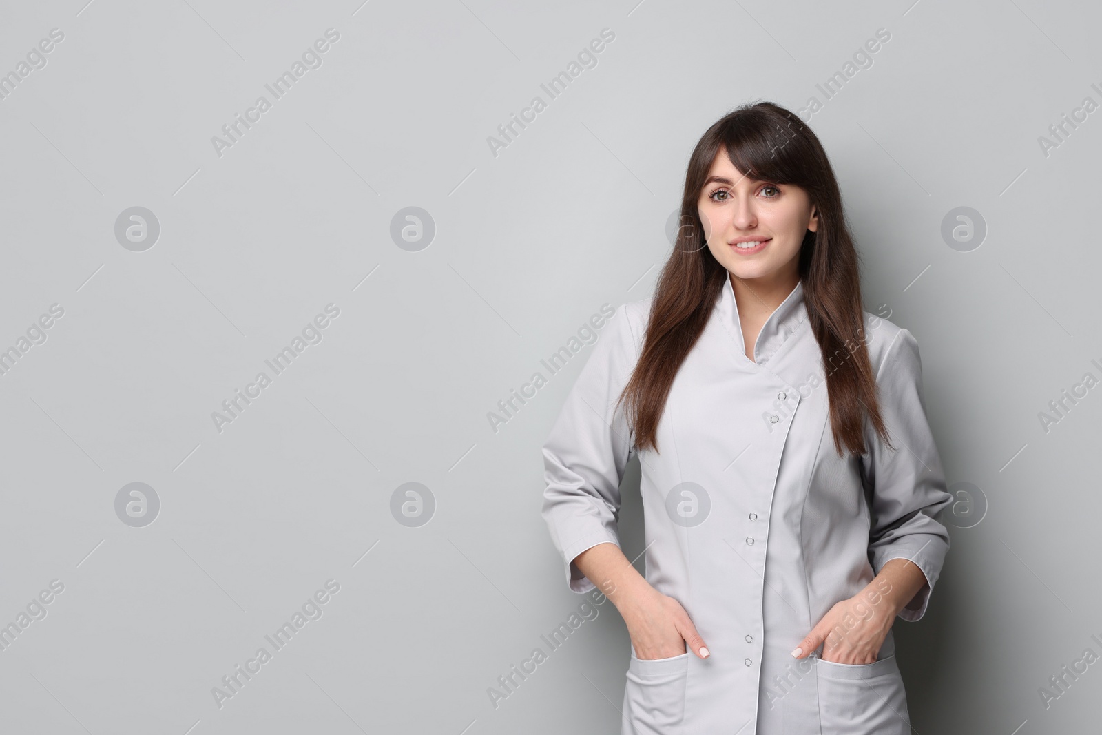 Photo of Cosmetologist in medical uniform on grey background, space for text