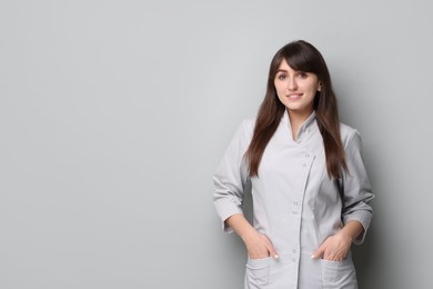 Cosmetologist in medical uniform on grey background, space for text