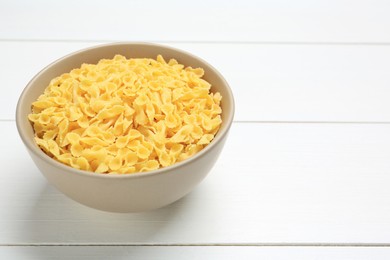 Photo of Raw farfalline pasta in bowl on white wooden table, closeup. Space for text