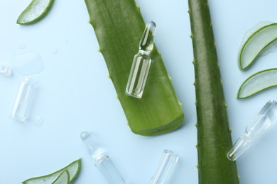 Flat lay composition with skincare ampoules and aloe leaves on light blue background