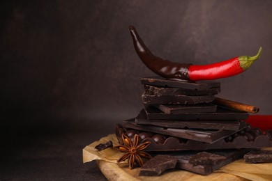 Photo of Red hot chili pepper and pieces of dark chocolate with spices on black table, space for text