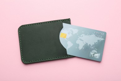 Leather card holder with credit card on pink background, top view