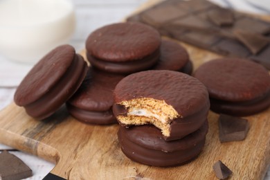 Tasty choco pies and pieces of chocolate on wooden board, closeup