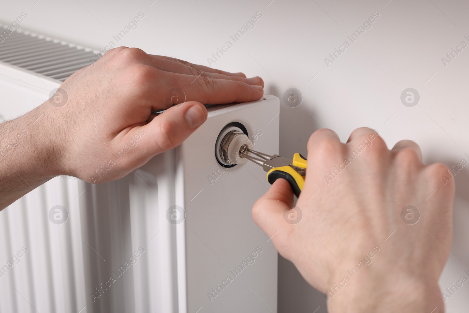 Photo of Professional repairman fixing heating radiator with pliers indoors, closeup