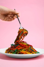 Photo of Woman eating delicious spaghetti painted with different food colorings on pink background, closeup