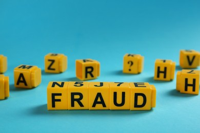 Photo of Word Fraud of yellow cubes with letters on light blue background