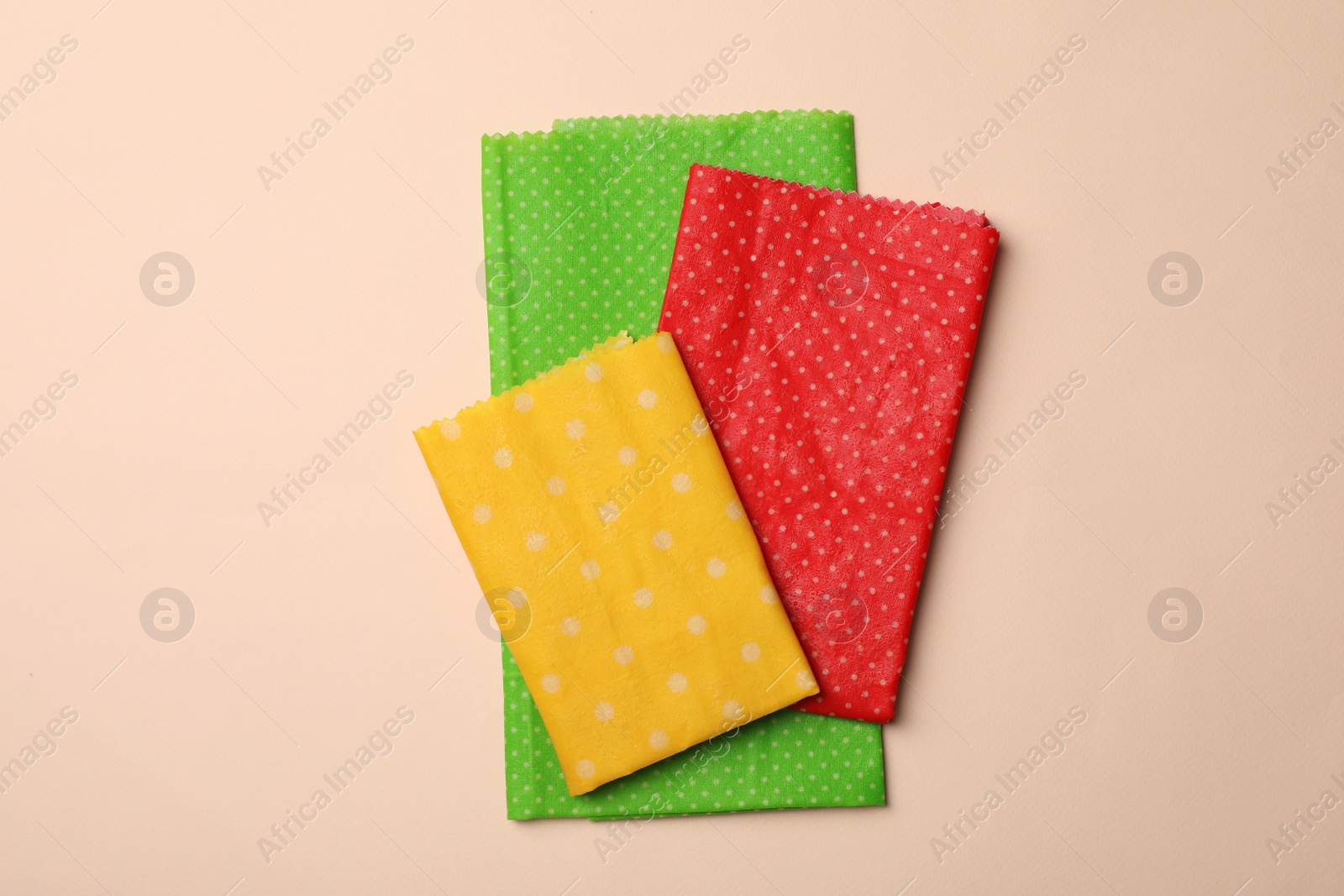 Photo of Colorful reusable beeswax food wraps on beige background, top view