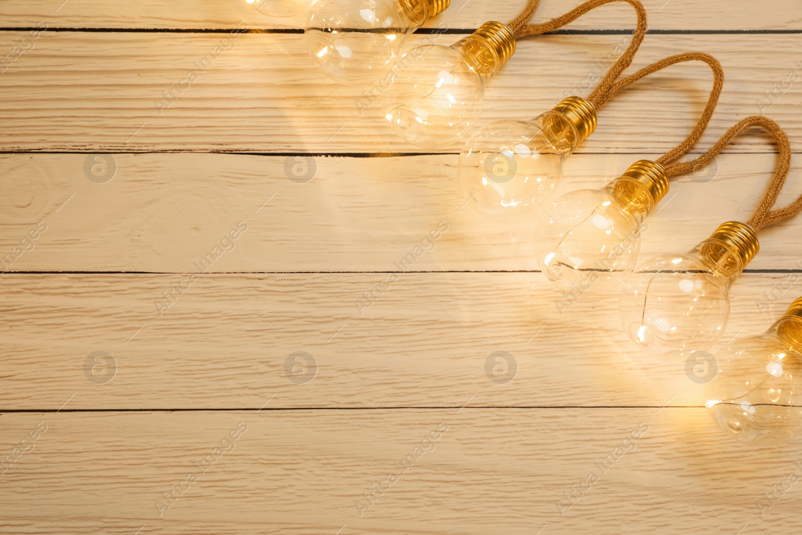 Photo of String lights with lamp bulbs on wooden background, top view. Space for text