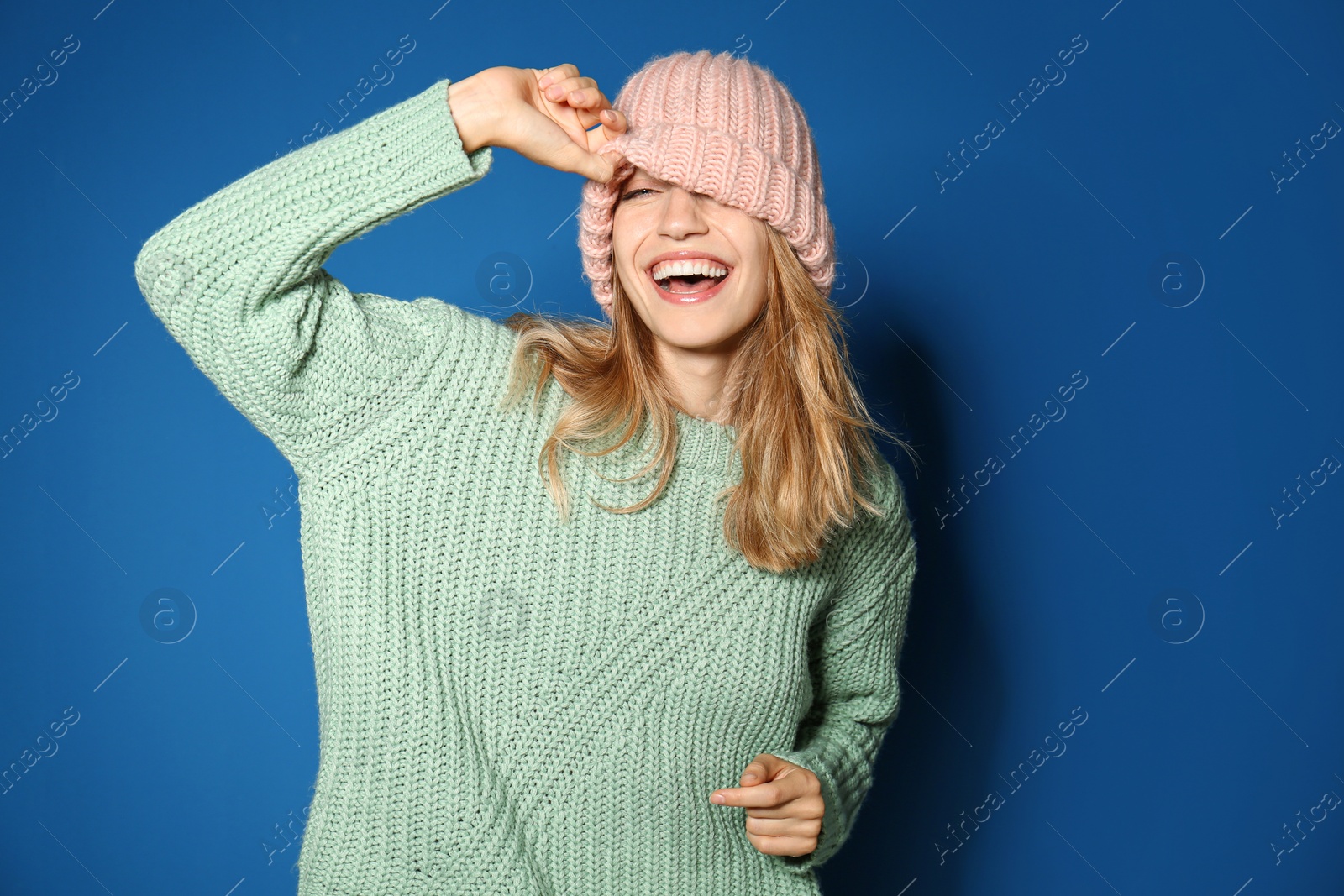 Image of Happy young woman wearing warm sweater and knitted hat on blue background