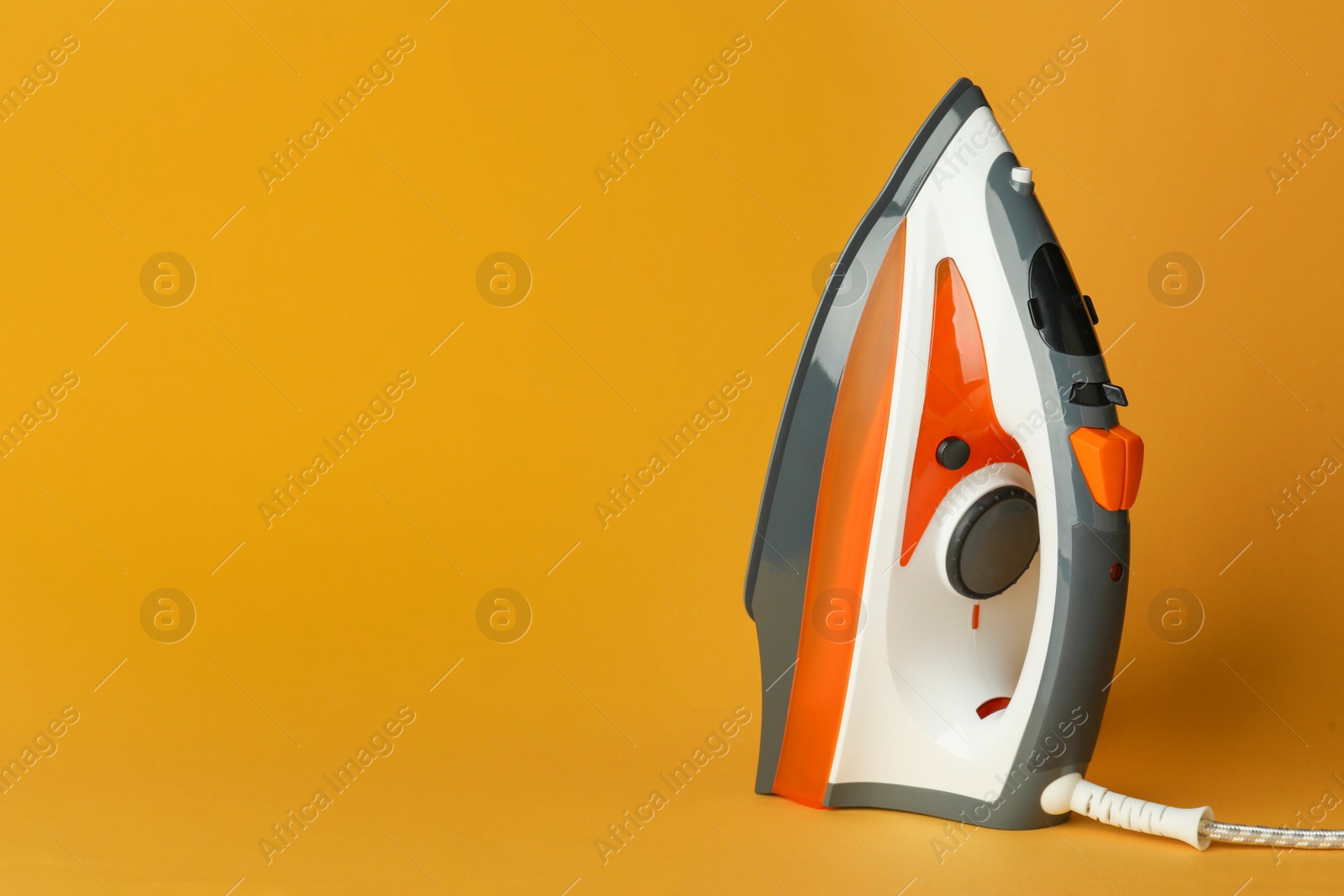 Photo of One modern iron on orange background, space for text. Home appliance